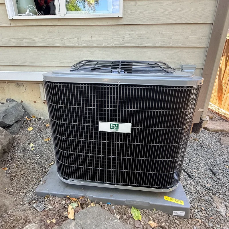 Air conditioner condenser on a gravel bed beside a wooden fence