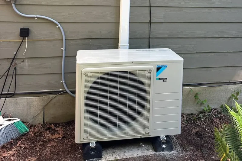 Daikin outdoor unit installed on levelling feet beside a downspout