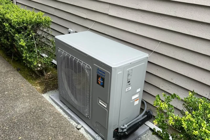 Heat pump outdoor unit installed between shrubs beside a home