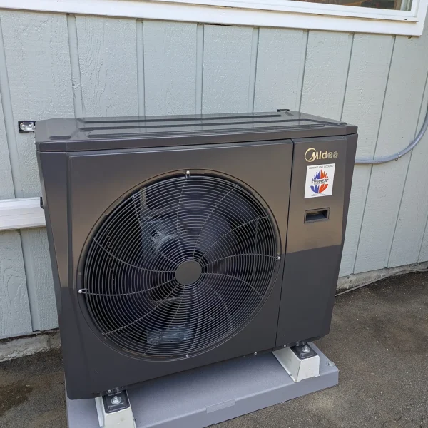 Midea heat pump on a pad against white board siding