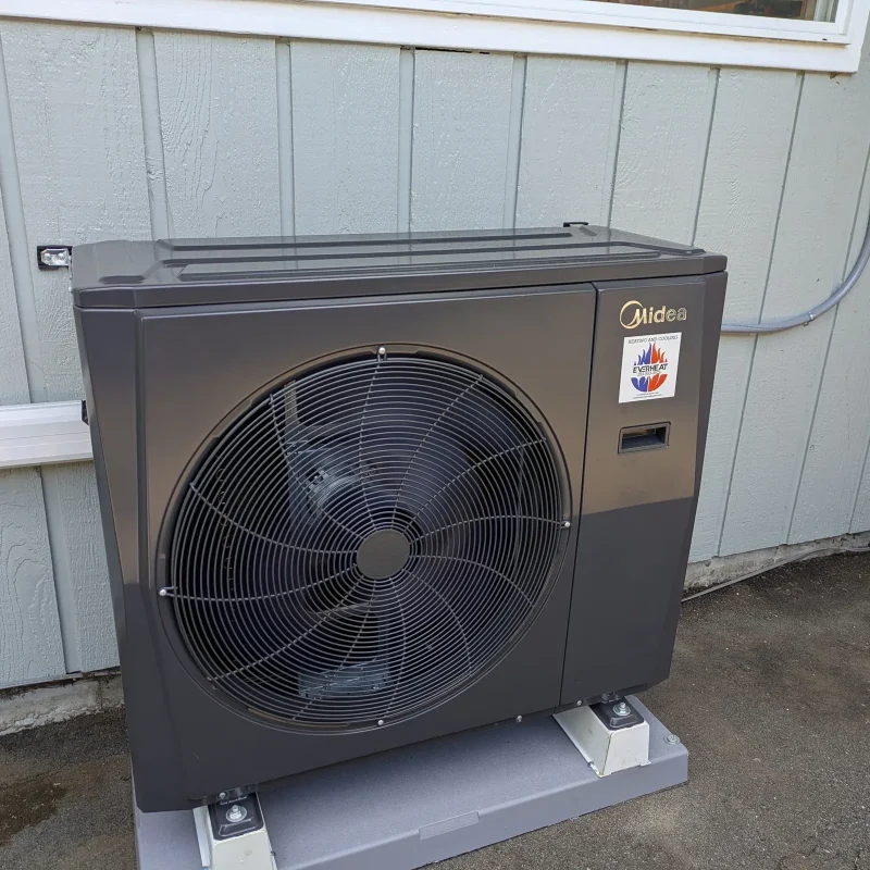 Midea heat pump on a pad against white board siding