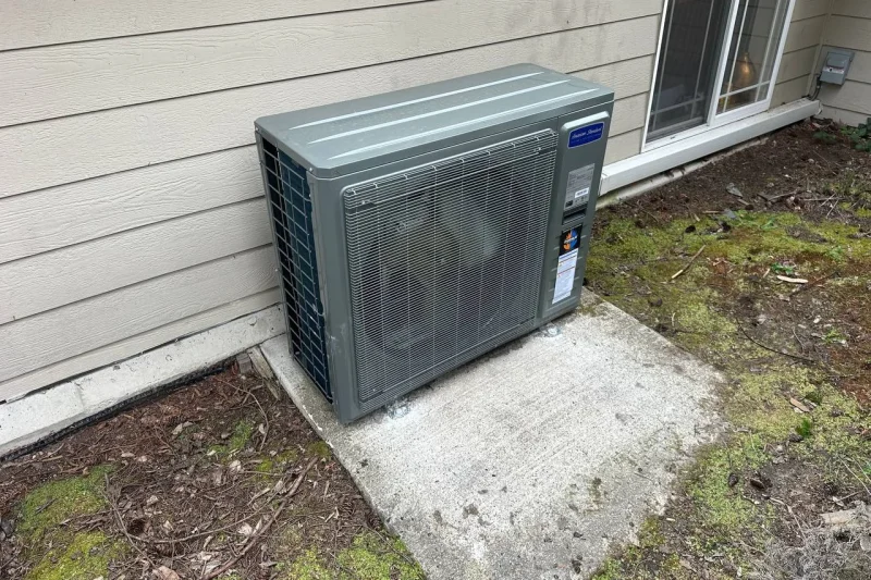Mini-split outdoor unit installed on a concrete pad beside cream siding