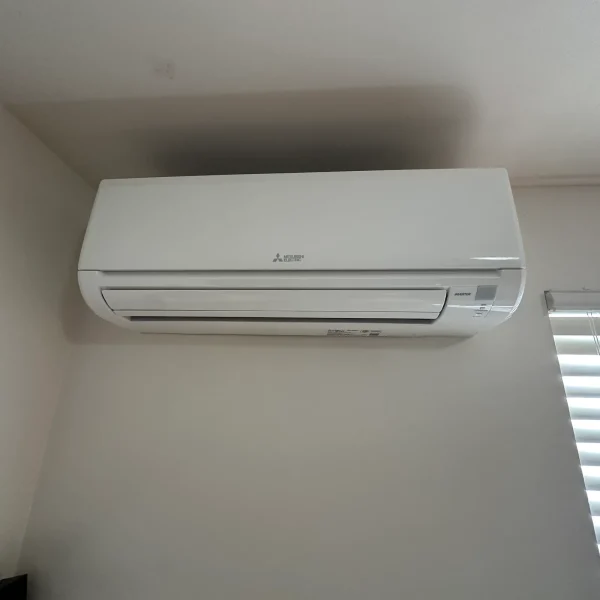 Mitsubishi mini-split indoor head beside a window with blinds