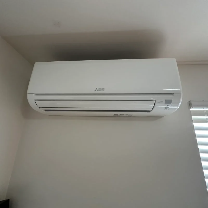 Mitsubishi mini-split indoor head beside a window with blinds