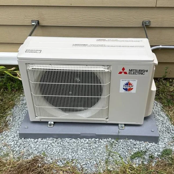 Mitsubishi ductless mini-split outdoor unit on a gravel pad beside a home