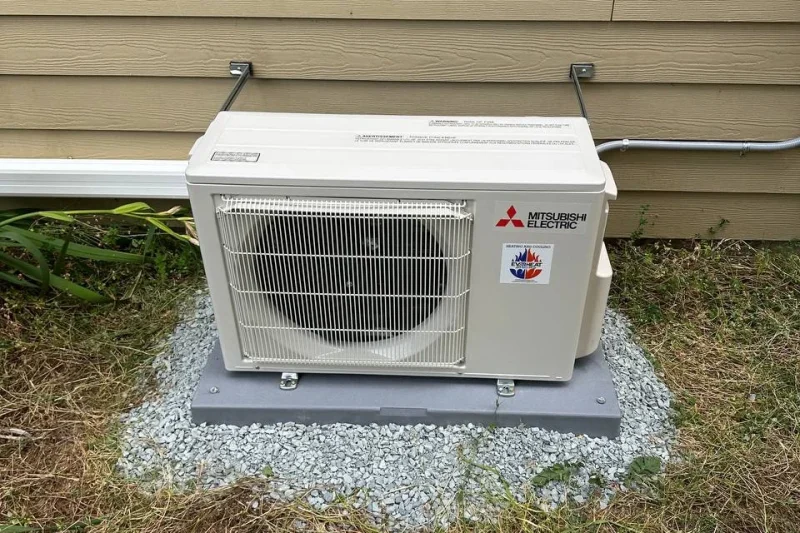 Mitsubishi ductless mini-split outdoor unit on a gravel pad beside a home