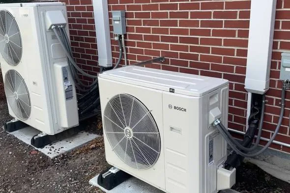 Two outdoor units installed side by side against a brick wall